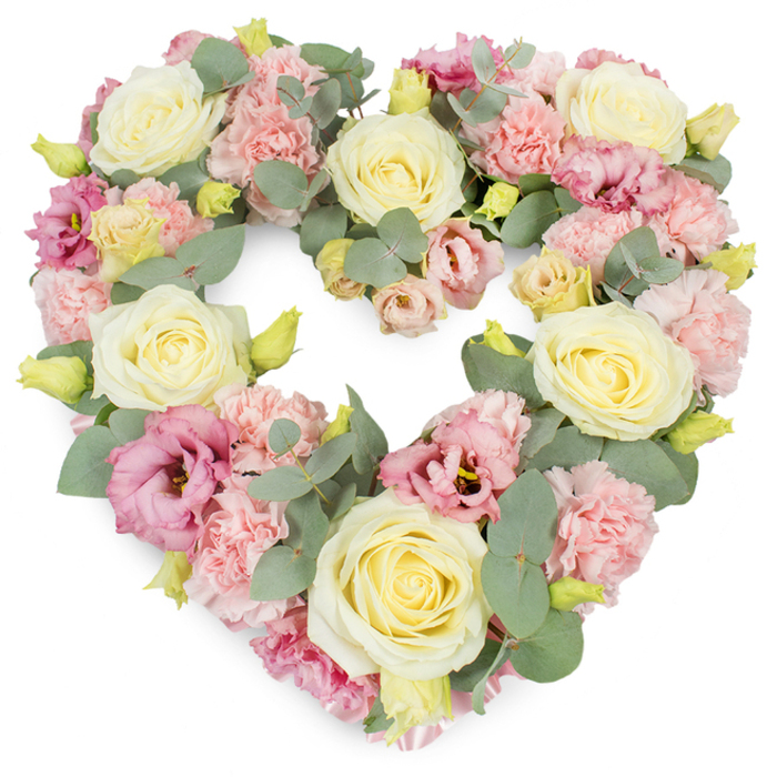A beautifully balanced, heart-shaped floral tribute fills the image, its soft colours standing out clearly against a bright white background. The heart is generously proportioned and completely filled with flowers, so the viewer sees only layers of petals and leaves, no supporting frame. Cream and buttery-yellow roses serve as the main focal flowers, each one at a perfect stage of openness, with petals spiralling outward in even, velvety layers that catch the light with a gentle sheen. Nestled among them are clusters of delicate, light pink carnations, their finely serrated petals building up in dense, ruffled mounds that lend the wreath a cosy, cushioned feel. Woven through these blooms are lisianthus in slightly deeper pink and mauve tones, their softer, more relaxed blossoms opening like small trumpets and adding contrast in both shape and shade. All around, sprigs of silvery-green eucalyptus are threaded into the composition, their round, matte leaves introducing a cool, calming element and helping to define the gentle curves of the heart. Tiny yellow-green buds appear intermittently, suggesting the freshness of newly cut stems and a sense of life continuing. The atmosphere of the arrangement is tender and composed, ideal for expressing sympathy and remembrance at a funeral or memorial in Ickenham, perhaps for a family gathering near Swakeleys Lake or a quiet service in one of the village's historic churches. This is the kind of carefully crafted tribute a local florist would create when asked to convey love, respect, and gratitude in a single, graceful gesture.