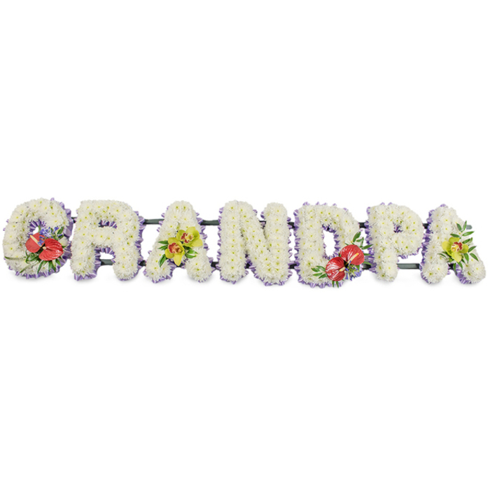 Against a clean, neutral white backdrop, a long, horizontal floral tribute spells out GRANDPA in solid, three-dimensional block letters, crafted with the care and precision of a professional florist familiar with the quiet, family-focused streets of Ickenham. Each letter is entirely covered with tightly packed white chrysanthemums, their neat, rounded petals overlapping to form plush, cushion-like panels that radiate simplicity, peace, and comfort. A slim border of soft lavender ribbon trims the base of every letter, offering a subtle wash of cool colour that outlines the shapes and adds refinement without disrupting the purity of the white flowers. The entire word rests on dark green support bars, glimpsed only at the edges, signalling the sturdy framework that keeps the tribute secure as it's moved from the workshop to a church service or graveside gathering around Ickenham or nearby Ruislip. Splashes of colour appear where accent sprays have been artfully arranged to personalise the tribute. On the 'G' and the 'D', deep red anthuriums with their glossy, heart-shaped spathes and golden-yellow spadices are nestled among dark, polished foliage and hints of delicate purple filler blooms, drawing the eye and suggesting strong, enduring love and gratitude. On the first 'A' and the last 'A', clusters of yellow-green orchids arc gently over the chrysanthemums, their graceful petals and fresh green tones offering a sense of quiet hope and lasting beauty. The overall composition is both serene and expressive, a bespoke sympathy design that could be ordered for a beloved grandfather's funeral, perhaps delivered along Long Lane or to a peaceful service near Ickenham's village centre, speaking softly of memories shared and a life well loved.