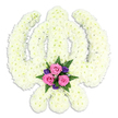 A reverent Sikh Khanda floral arrangement dominates the image, its iconic silhouette perfectly captured against a smooth white backdrop, much like the calm interiors of local service spaces around Ickenham. The Khanda's three main components - the upright double-edged sword in the centre, the embracing circular chakkar, and the two gently arched kirpans that cross and flare outwards - are entirely formed from closely clustered white or cream chrysanthemums. Their small, feathery petals overlap to create a thick, cushioned texture, lending softness to the otherwise strong and symbolic lines of the emblem. The white blooms reflect the light evenly, suggesting purity, peace, and a spiritual stillness that feels appropriate for a funeral or memorial. At the very bottom of the piece, framed neatly between the handles of the kirpans, a compact spray of coloured flowers draws the focus. Several pink roses, open enough to reveal their swirling centres, sit at the heart of this cluster, representing love and gentle remembrance. They are surrounded by rich purple blossoms and fresh green fern fronds, whose delicate, lacy leaves extend slightly over the white base, adding a touch of natural movement. Subtle, soft lighting ensures that every detail is clearly visible, casting only a faint shadow beneath the design to suggest one's hand could slide just beneath the lower curve. This floral Khanda tribute has an air of calm strength and quiet devotion, the kind of carefully arranged piece chosen by Sikh families in Ickenham when they wish to honour a loved one's beliefs and life story with a meaningful, beautifully composed final gesture.