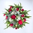 Viewed from directly above against a spotless white background, this abundant bouquet forms a rich, circular dome of colour, as if it has just been set down on a florist's bench in Ickenham. Deep crimson roses are clustered at the centre, some still tightly budded, others loosening into layered, velvety spirals that suggest romance and quiet luxury. Around them, ruffled carnations in vibrant ruby and fuchsia tones create a lively halo, their frilled petals catching the light and adding a sense of movement and celebration. Threaded between the bold reds, small white spray chrysanthemums and daisy-like blooms dot the arrangement with crisp, clean brightness, giving the eye places to rest. Tiny white gypsophila, or baby's breath, float delicately through every gap, like a fine mist or scattered stars, softening the transitions between flowers. Supporting this cloud of colour is a generous collar of greenery: pointed dark green leaves, possibly from lilies or alstroemeria, fan outward to give structure and depth, while rounded, silvery eucalyptus leaves weave through the bouquet, their cool blue-green cast lending a contemporary touch. The overall impression is of a hand-crafted, full-bodied bouquet made for heartfelt gifting across Ickenham, whether delivered to a home near Swakeleys Park or a cosy café off Long Lane. The colour palette of passionate reds, pure whites, and fresh greens makes the bouquet perfectly suited to anniversaries, Valentine's Day, or a special birthday, but it would also feel at home as a thoughtful get-well gesture. Everything about the arrangement, from the careful choice of textures to the balanced distribution of colour, speaks to the steady hands and practiced eye of an experienced local florist.